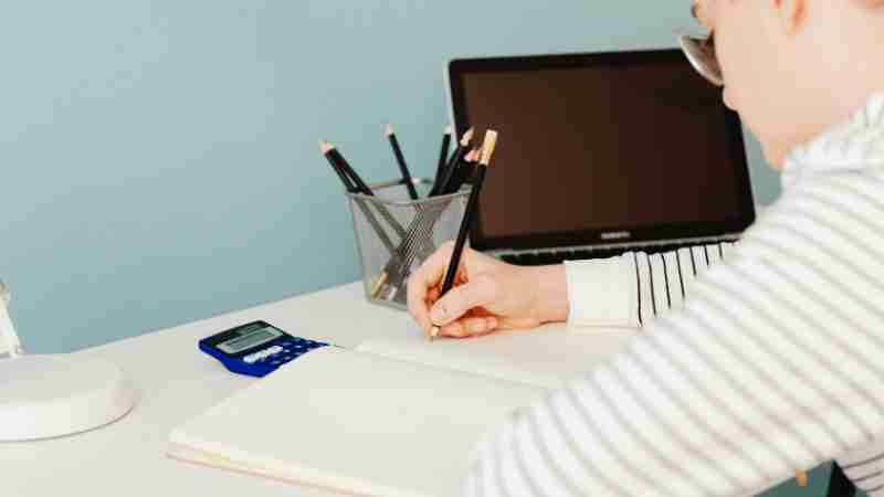 Young adult writing with pencils at a desk with laptop and calculator, perfect for study and work themes., tags: und die - pexel